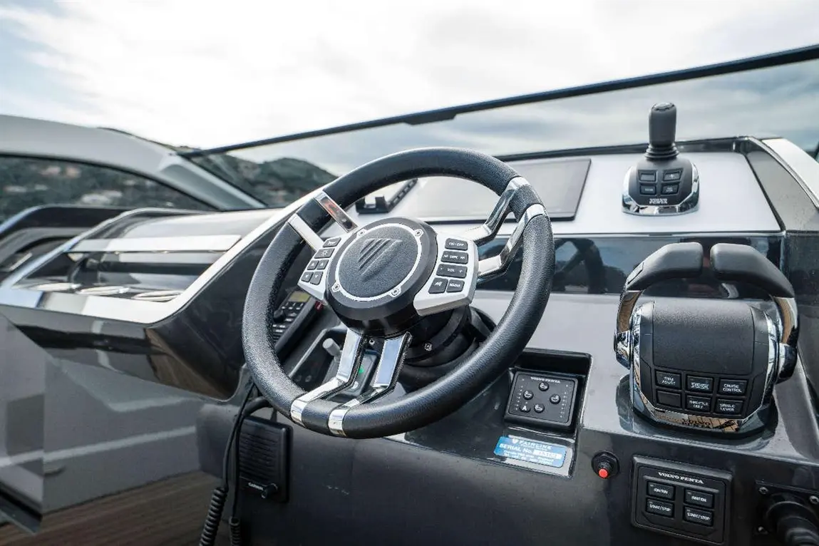 Boat dashboard featuring a steering wheel and control panel with navigation buttons, set against a cloudy sky.
